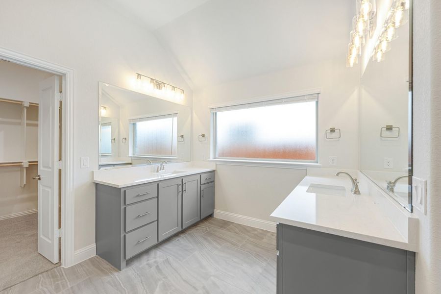 Master bathroom with gray cabinets, white countertops, soaking tub, and walk-in closet access Master bathroom with gray cabinets, white countertops, soaking tub, and walk-in closet access