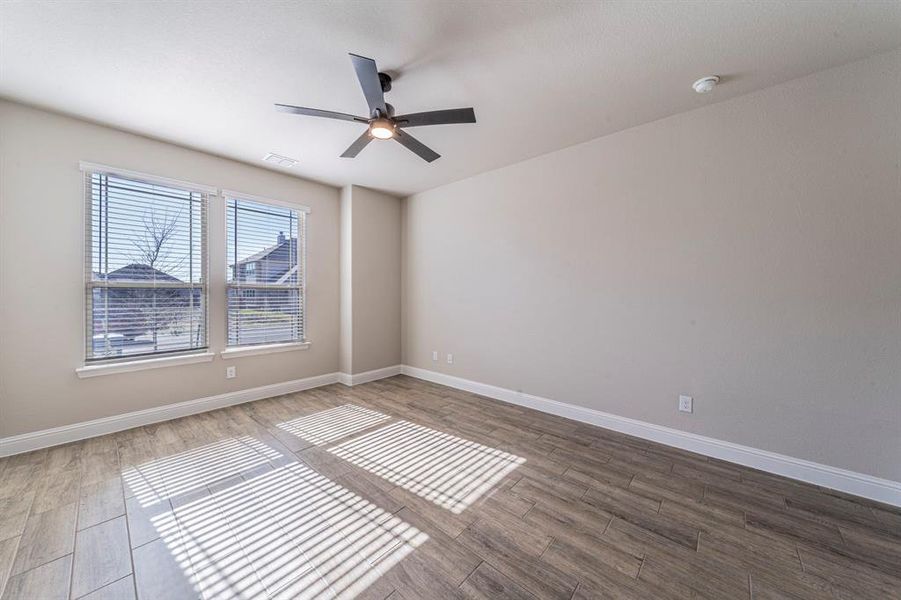 Spacious room featuring wood-finish flooring, two large windows with blinds, a ceiling fan with integrated lighting, and neutral wall tones