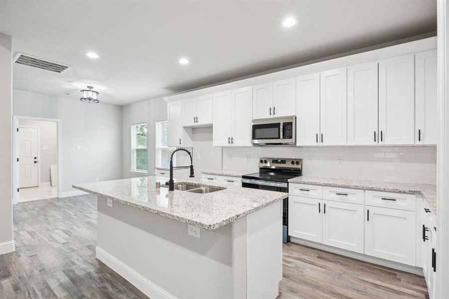 Kitchen with white cabinetry, appliances with stainless steel finishes, a kitchen island with sink, light stone countertops, and backsplash