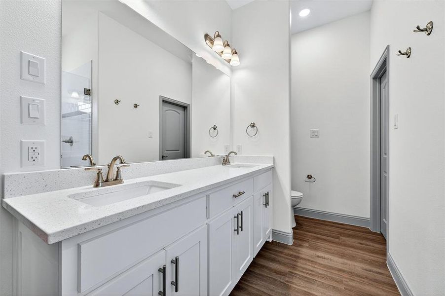 Full bath featuring double vanity, dark wood finished floors, and a shower stall