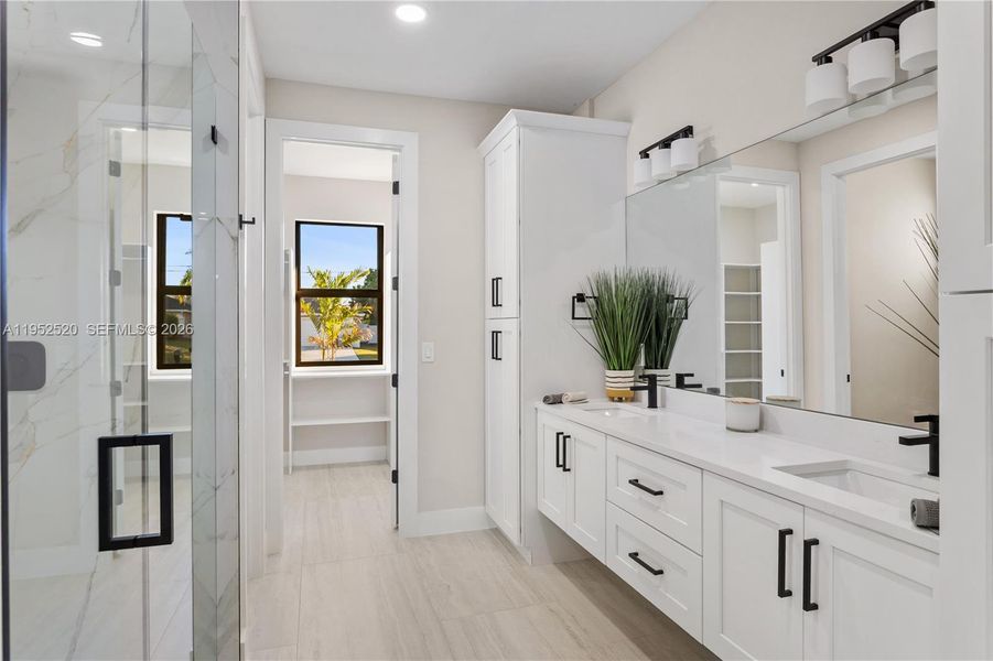 Dual-sink vanity w/ quartz countertops, sleek white cabinetry & contemporary lighting complements the spa-like design.