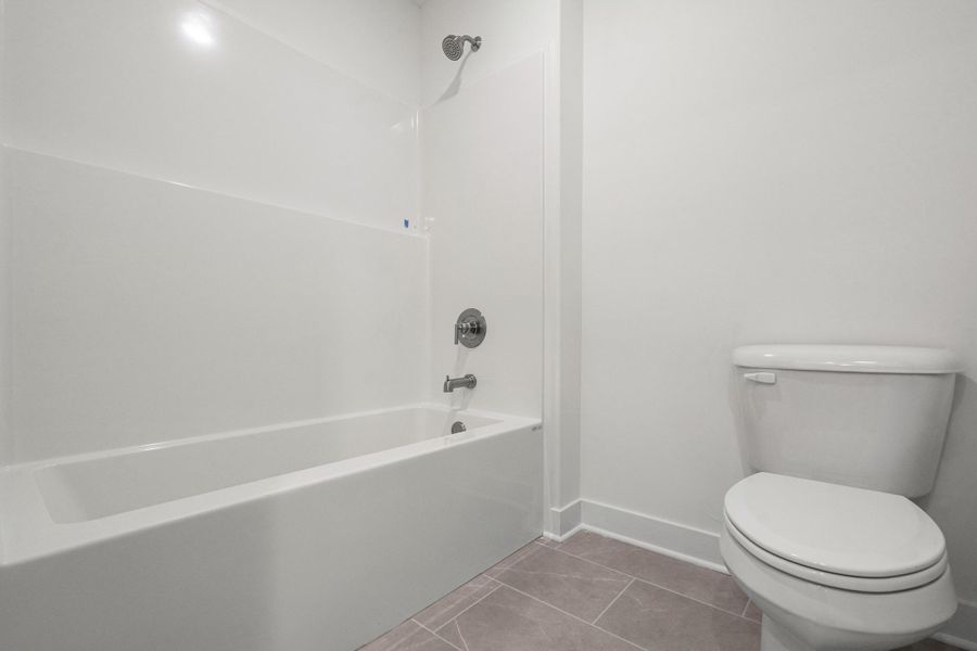 White bathtub and shower combination with chrome fixtures, paired with a white toilet, set against light gray floor tiles