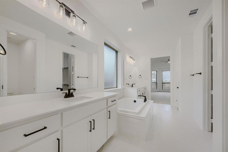 Spacious bathroom featuring dual vanities with white cabinetry and countertops, a large soaking tub with matte black fixtures, and modern overhead lighting