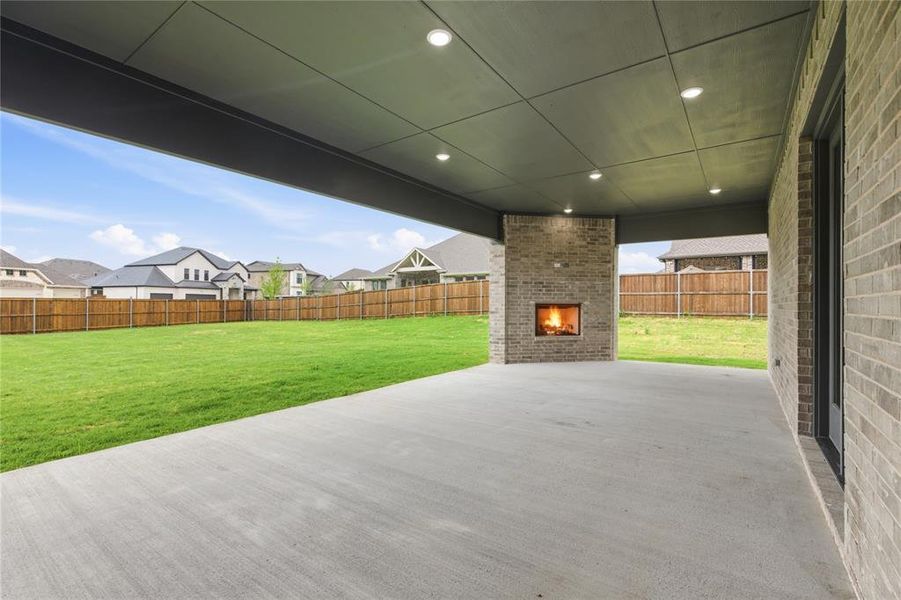 Covered outdoor patio featuring a brick-clad fireplace, recessed lighting, concrete flooring, and an expansive lawn Covered outdoor patio featuring a brick-clad fireplace, recessed lighting, concrete flooring, and an expansive lawn