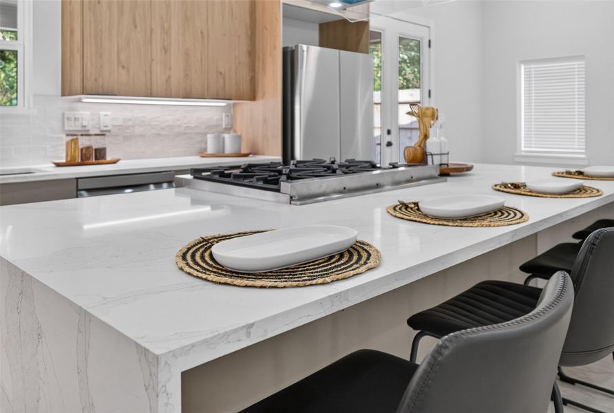Sleek modern kitchen featuring a large marble island with a built-in gas cooktop, elegant bar seating, and stylish wood cabinetry.
