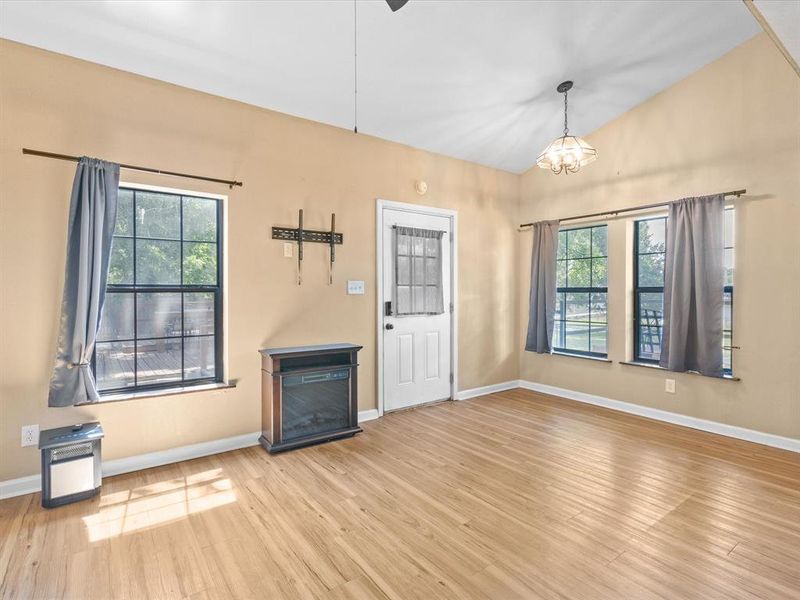 Unfurnished living room featuring plenty of natural light, wood finished floors, a chandelier, and vaulted ceiling Unfurnished living room featuring plenty of natural light, wood finished floors, a chandelier, and vaulted ceiling