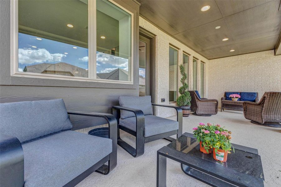 Spacious, covered patio featuring comfortable seating, a coffee table with plants, and stylish wicker furniture. The area is well-lit with recessed lighting and offers a relaxing outdoor space ideal for entertaining or unwinding. Spacious, covered patio featuring comfortable seating, a coffee table with plants, and stylish wicker furniture. The area is well-lit with recessed lighting and offers a relaxing outdoor space ideal for entertaining or unwinding.