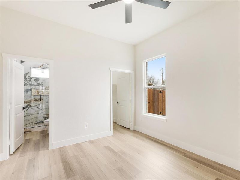 Unfurnished bedroom with light wood-style floors, ensuite bath, and a ceiling fan