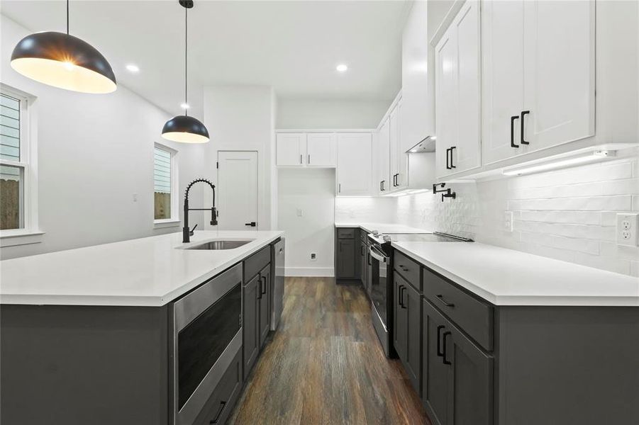 Kitchen with white cabinets, appliances with stainless steel finishes, a kitchen island with sink, decorative light fixtures, and dark wood finished floors
