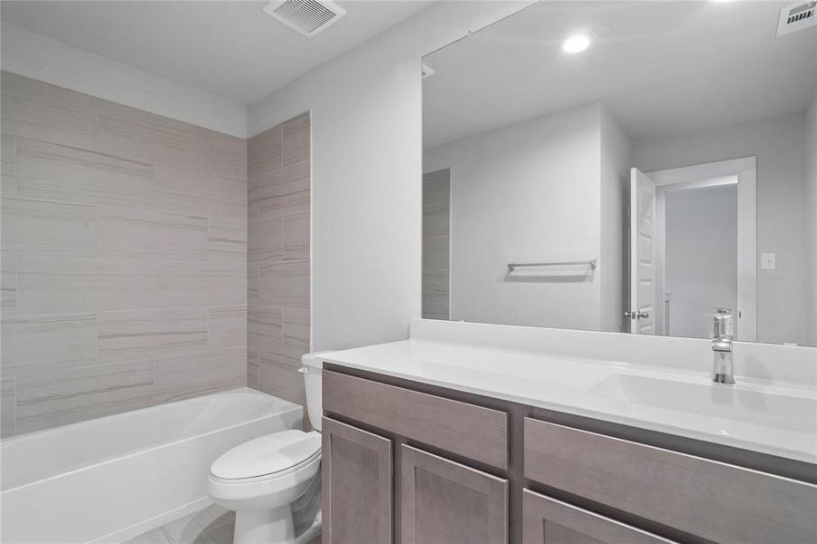 Secondary bath features tile flooring, bath/shower combo with tile surround, stained wood cabinets, beautiful light countertops, mirror, sleek fixtures and modern finishes.