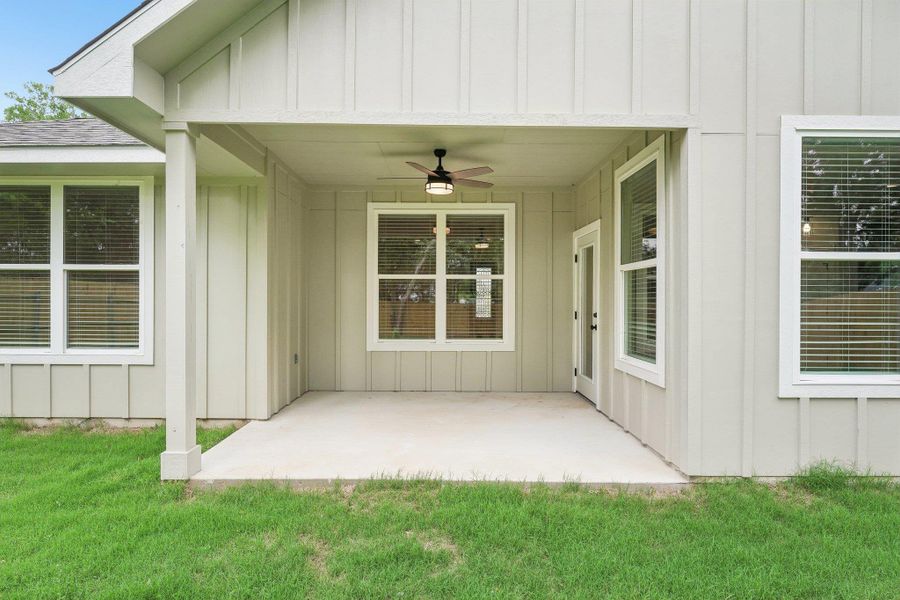 View of exterior entry featuring a patio, a yard, board and batten siding, and ceiling fan View of exterior entry featuring a patio, a yard, board and batten siding, and ceiling fan
