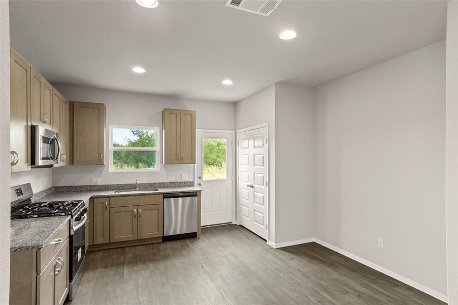 Kitchen featuring appliances with stainless steel finishes, wood finished floors, recessed lighting, and light stone counters