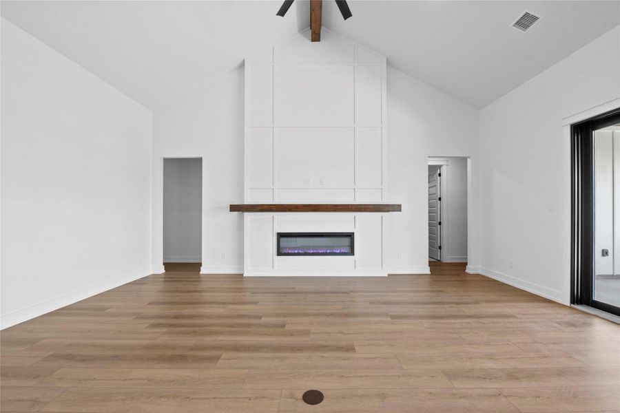 Unfurnished living room featuring beamed ceiling, light wood finished floors, high vaulted ceiling, an electric fireplace, and ceiling fan Unfurnished living room featuring beamed ceiling, light wood finished floors, high vaulted ceiling, an electric fireplace, and ceiling fan