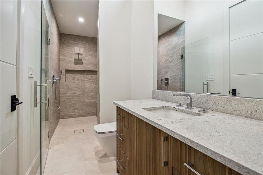 The Guest Bathroom offers a long vanity providing ample space for getting ready, featuring an undermount sink, storage drawers, and cabinets below. It includes a walk-in shower with custom shower niches and a seamless glass shower door, combining practicality with a touch of luxury for guests.