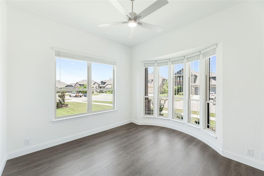 Empty room with dark hardwood floors, ceiling fan, and large bay windows overlooking a neighborhood Empty room with dark hardwood floors, ceiling fan, and large bay windows overlooking a neighborhood