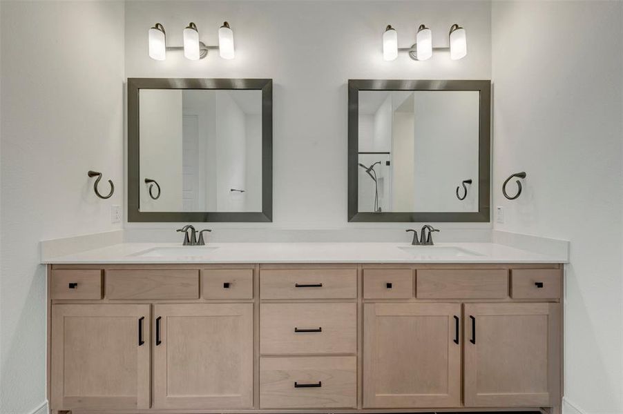Dual vanity featuring undermount sinks, light wood-finish cabinetry, matte black hardware, white countertops, and framed mirrors with brushed nickel light fixtures Dual vanity featuring undermount sinks, light wood-finish cabinetry, matte black hardware, white countertops, and framed mirrors with brushed nickel light fixtures