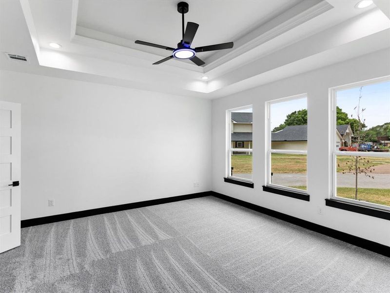 Spacious room featuring a tray ceiling with recessed lighting, black modern ceiling fan, three pane windows, white walls, and gray patterned carpeting