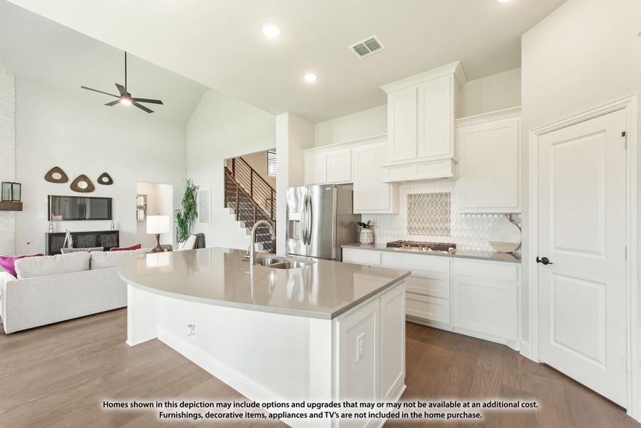 Open-concept kitchen with white cabinets, large island, and stainless steel fridge, open to living room with high ceilings