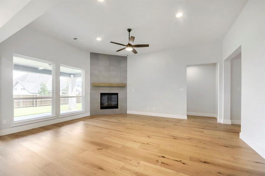 Spacious interior featuring wood-finish flooring, a contemporary fireplace with a stone-look surround and wood mantel, recessed lighting, and a ceiling fan