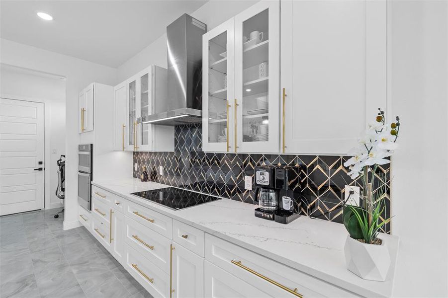 Sleek kitchen featuring white cabinetry with gold-tone hardware, a black geometric tile backsplash, and light-toned countertops