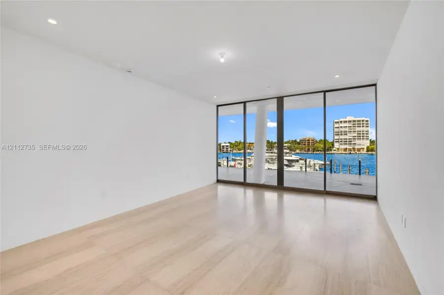 Floor-to-ceiling glass sliding doors, wood-finish flooring, recessed lighting, and water frontage
