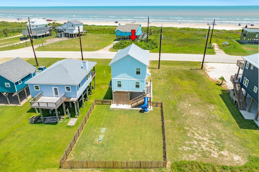 Aerial perspective highlights the property's location just across from the beach, with a fenced yard and convenient access to the shoreline.