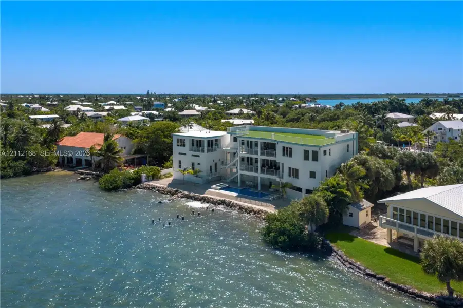 Waterfront multi-story residence featuring a private pool, multiple tiered balconies, a rooftop terrace, and stone shoreline stabilization Waterfront multi-story residence featuring a private pool, multiple tiered balconies, a rooftop terrace, and stone shoreline stabilization