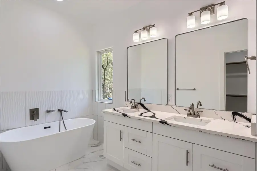 Bathroom with double vanity, marble look tile flooring, a soaking tub, and tile walls