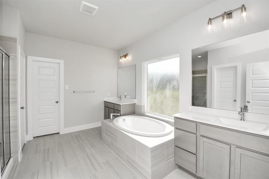 Escape to a spa-like oasis in this primary bathroom. Enjoy a walk-in showerwith tile surround, a separate garden tub with custom detailing, and an elegantvanity featuring light countertops, modern hardware, and beautiful vanity lights.Experience luxury and relaxation in every detail.