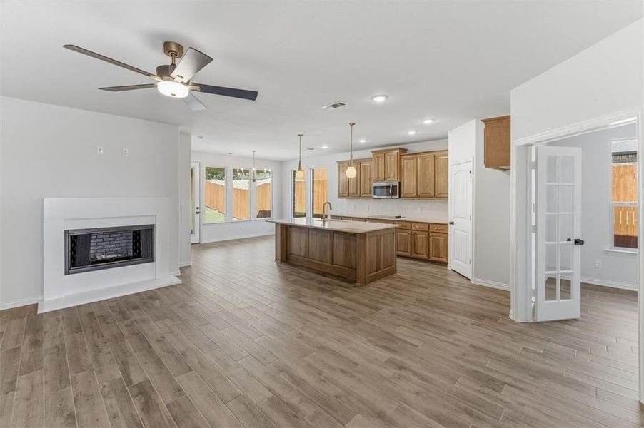 Kitchen featuring open floor plan, light countertops, a fireplace, a kitchen island with sink, and ceiling fan
