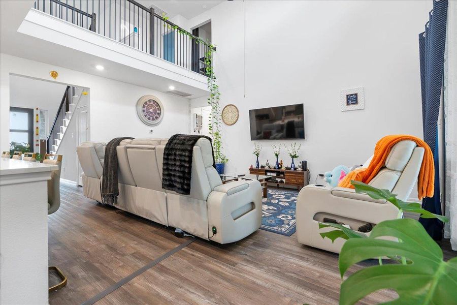 Living room with wood finished floors, stairway, and a high ceiling
