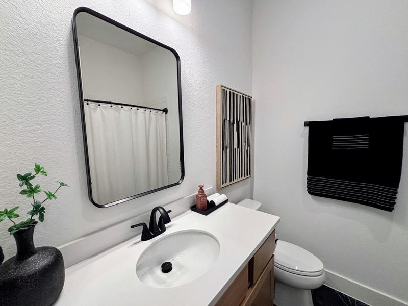 This modern bathroom #2 features a sleek design with a large rectangular mirror, stylish black fixtures, and a white countertop.