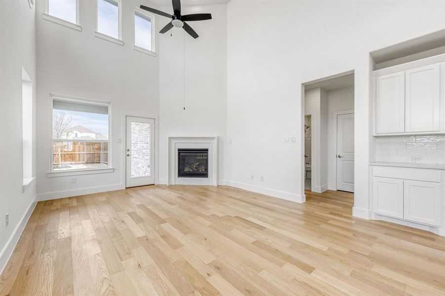 Unfurnished living room with light wood-style floors, ceiling fan, a high ceiling, and a glass covered fireplace