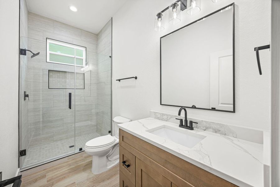 This modern bathroom features a glass-enclosed shower with sleek tilework, a large mirror, and contemporary lighting. The black fixtures and marble countertop add a touch of elegance, while the neutral color palette provides a clean, sophisticated look.