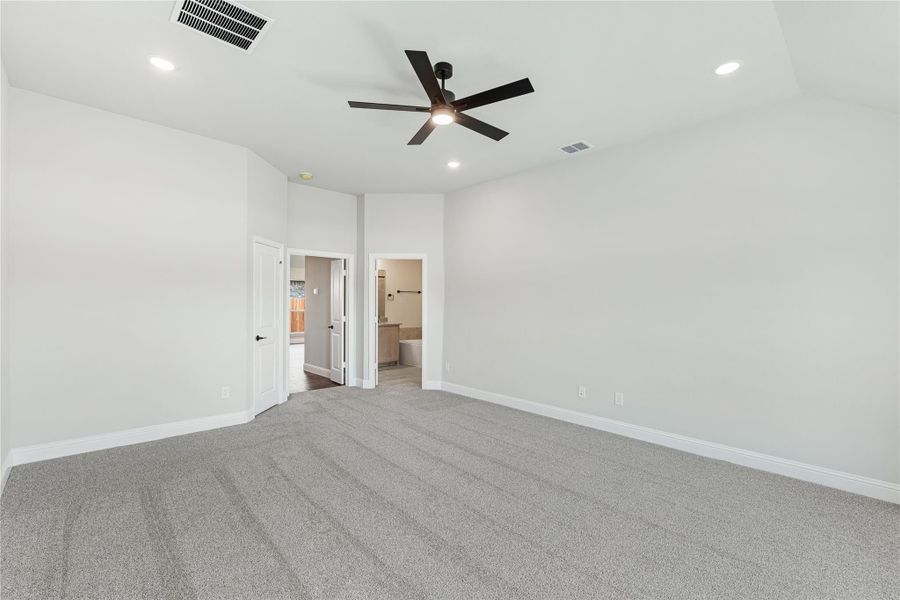 Spacious bedroom with gray carpet, ceiling fan, and open doorway to ensuite bathroom Spacious bedroom with gray carpet, ceiling fan, and open doorway to ensuite bathroom