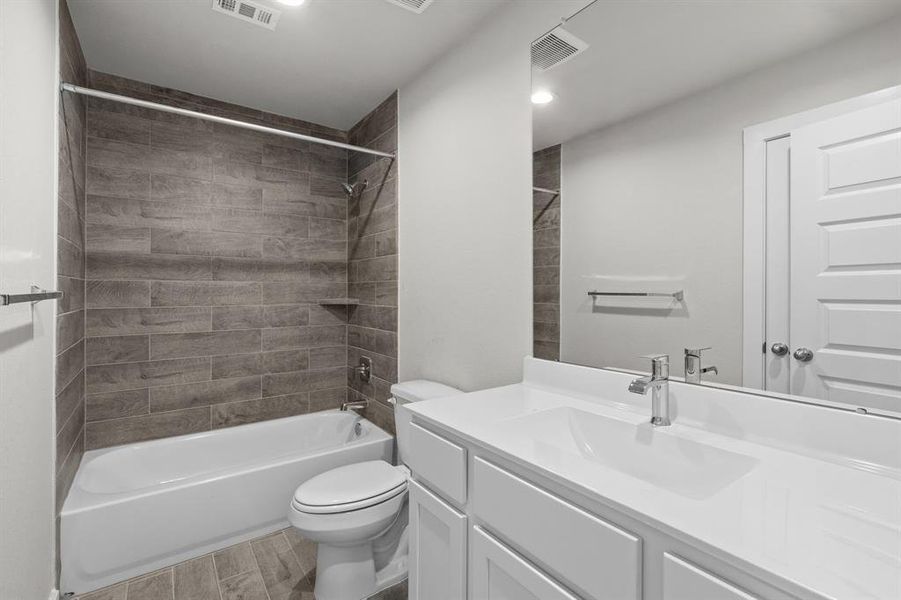 Indulge in refined charm in the secondary bathroom, where the tile flooring harmonizes with a bath/shower combo surrounded by tasteful tile. Light wood cabinets, coupled with a gorgeous countertop, elevate the space, cultivating a truly welcoming atmosphere. Sample photo of completed home with similar floor plan. As-built interior colors and selections may vary.