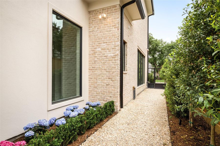Fully landscaped side yard with gravel pathway, lush greenery, and gated access.