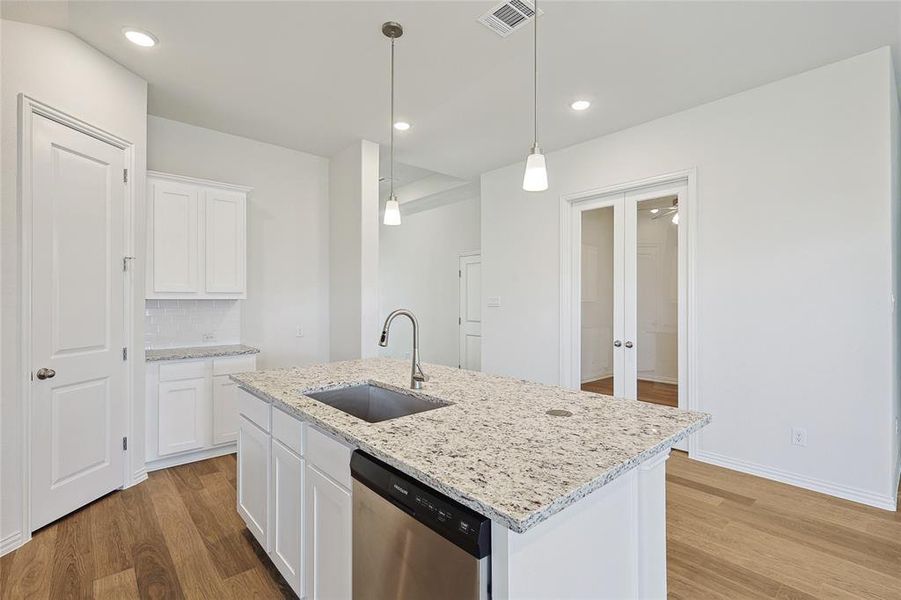 Kitchen with white cabinets, dishwasher, light hardwood / wood-style flooring, a center island with sink, and sink