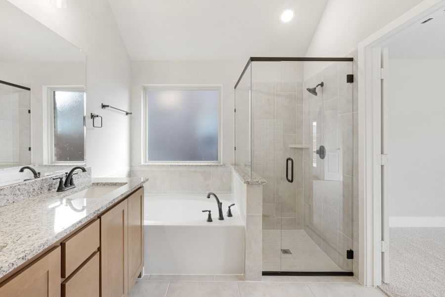 Master bathroom with double vanity, soaking tub, and glass-enclosed tile shower with dark fixtures