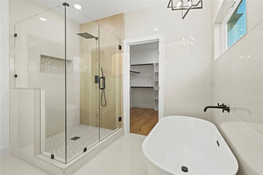 Bathroom featuring a spacious closet, a stall shower, a freestanding bath, and tile walls