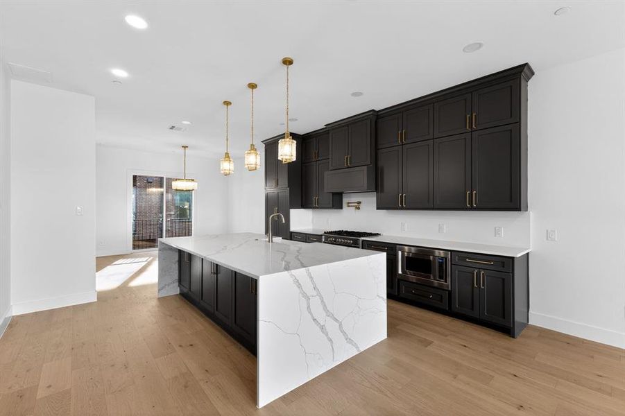 Kitchen with gray cabinets, light stone counters, a spacious island, light wood finished floors, and stainless steel microwave