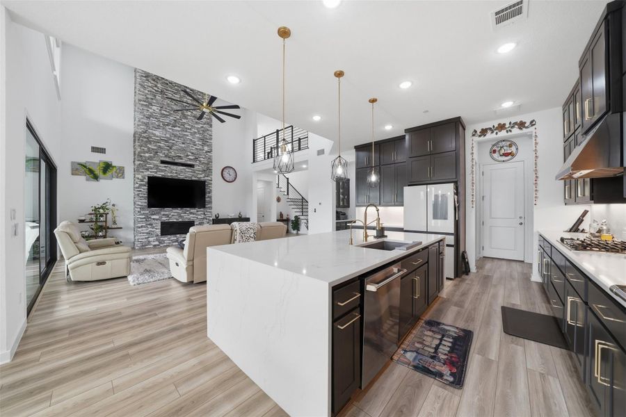 Open concept living space featuring a modern kitchen with dark cabinetry, an expansive island with a sink, and pendant lighting