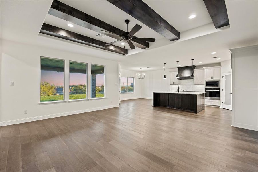 Unfurnished living room with beam ceiling, a chandelier, light wood-style flooring, a ceiling fan, and recessed lighting