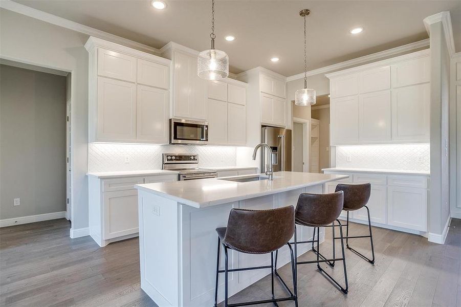 Kitchen with appliances with stainless steel finishes, sink, white cabinets, hanging light fixtures, and a center island with sink