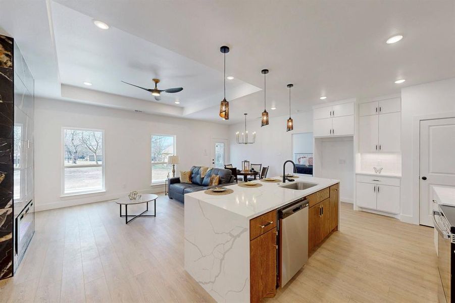 Kitchen with an island with sink, light stone countertops, a tray ceiling, dishwasher, and white cabinets