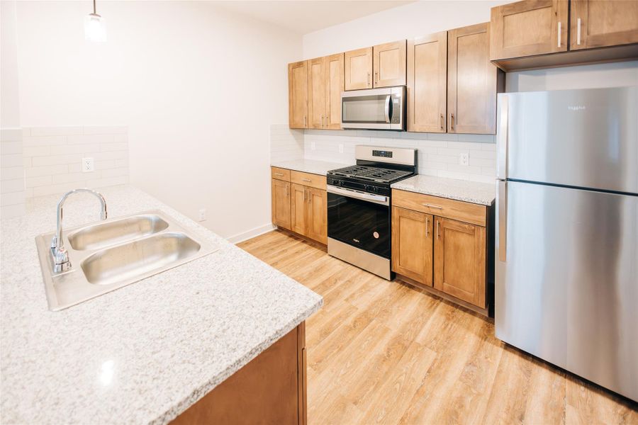 Kitchen with appliances with stainless steel finishes, light wood finished floors, decorative backsplash, decorative light fixtures, and light stone countertops