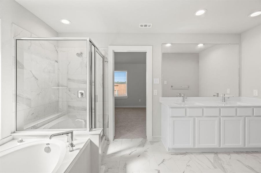 Experience luxury in this spa-like primary bathroom featuring a massive walk-in shower with tile surround. Wood cabinets with light countertops complement the space. Sample photo of completed home with similar floor plan. As-built interior colors and selections may vary.