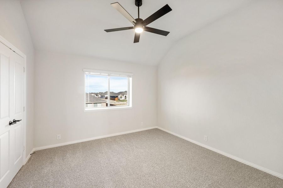 Empty bedroom with vaulted ceiling, black ceiling fan, carpet flooring, and a window overlooking the neighborhood. Empty bedroom with vaulted ceiling, black ceiling fan, carpet flooring, and a window overlooking the neighborhood.