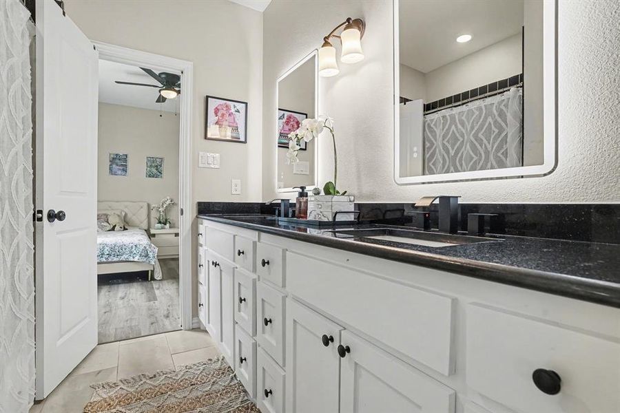 Jack and Jill bathroom featuring double vanity, a shower with shower curtain, light tile patterned flooring, and a textured wall