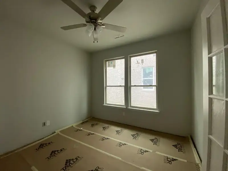 Room featuring neutral painted walls, two double-hung windows, a ceiling fan with integrated lighting, and a French door with multiple glass panes